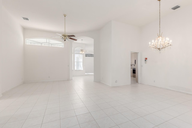 tiled spare room featuring ceiling fan with notable chandelier and a towering ceiling