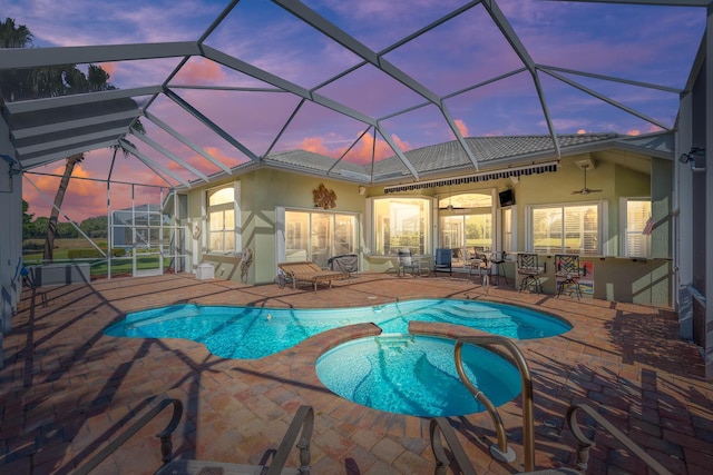 view of pool with glass enclosure, ceiling fan, a patio area, and an in ground hot tub