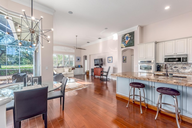 kitchen with light stone countertops, hanging light fixtures, stainless steel appliances, wood-type flooring, and white cabinets