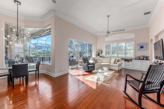 living room featuring plenty of natural light, wood-type flooring, ceiling fan with notable chandelier, and ornamental molding