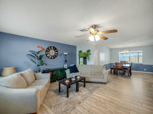 living room featuring ceiling fan with notable chandelier, a textured ceiling, and light hardwood / wood-style flooring