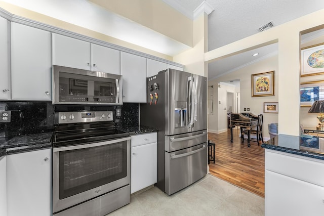 kitchen with white cabinets, vaulted ceiling, decorative backsplash, dark stone countertops, and stainless steel appliances