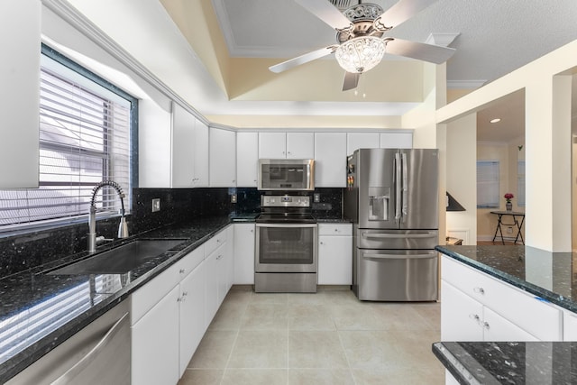 kitchen featuring tasteful backsplash, dark stone counters, stainless steel appliances, sink, and white cabinetry