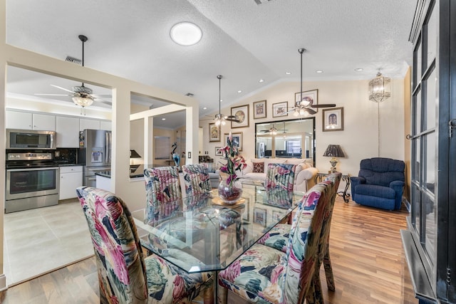 dining room with an inviting chandelier, light wood-type flooring, a textured ceiling, and vaulted ceiling