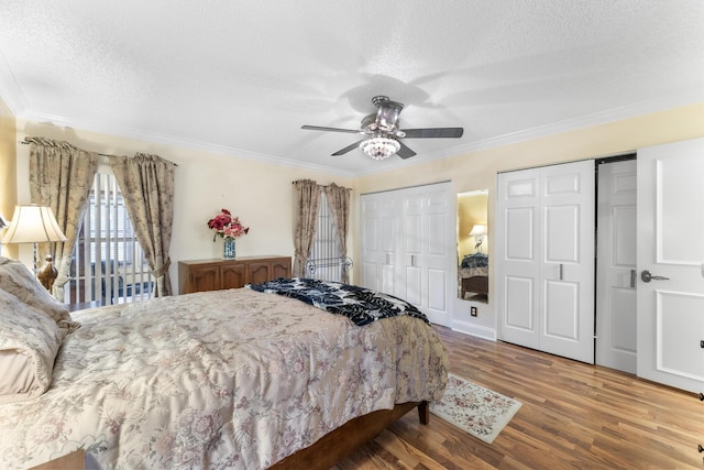 bedroom featuring ornamental molding, a textured ceiling, ceiling fan, wood-type flooring, and multiple closets