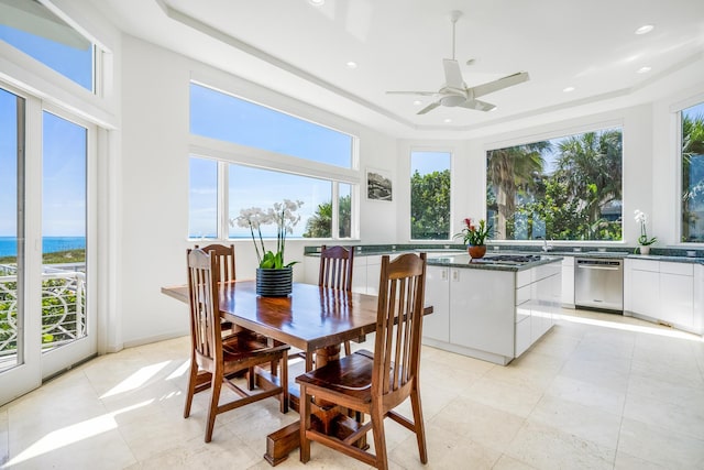 tiled dining room featuring a raised ceiling, ceiling fan, and a water view