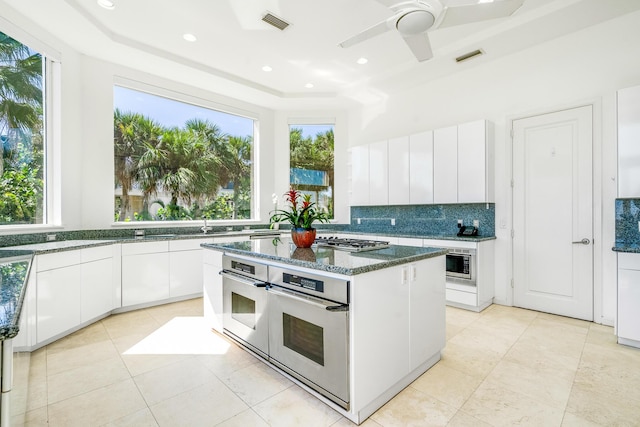 kitchen featuring stainless steel appliances, a kitchen island, tasteful backsplash, dark stone counters, and white cabinets