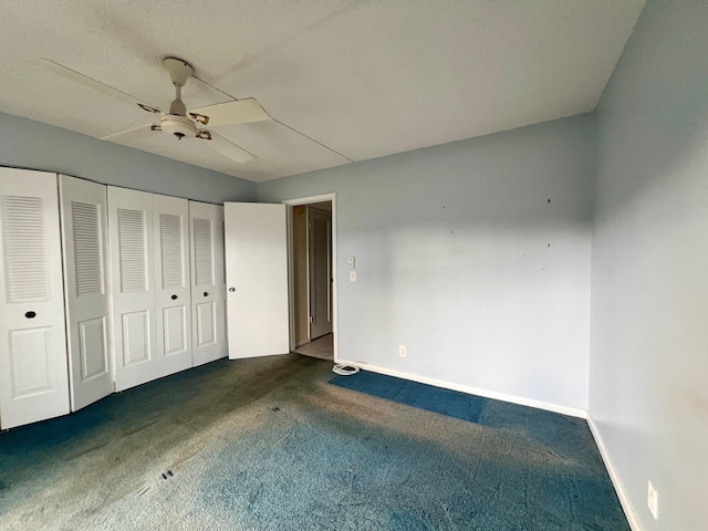 unfurnished bedroom with ceiling fan, dark carpet, and a closet