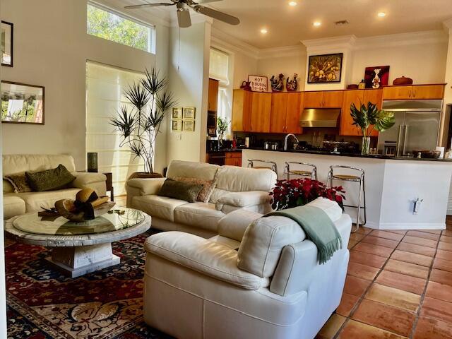 living room with ceiling fan, sink, a high ceiling, crown molding, and light tile patterned floors