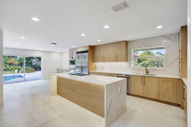 kitchen with tasteful backsplash, light stone counters, stainless steel appliances, sink, and a center island