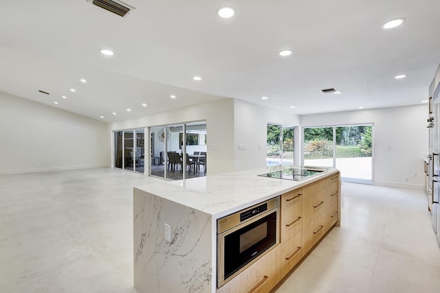 kitchen featuring black electric stovetop, light brown cabinetry, light stone counters, and a spacious island