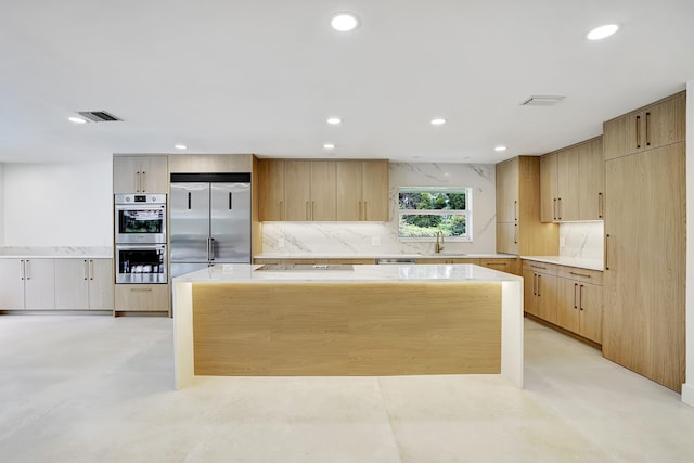 kitchen with a center island, sink, decorative backsplash, light brown cabinetry, and appliances with stainless steel finishes