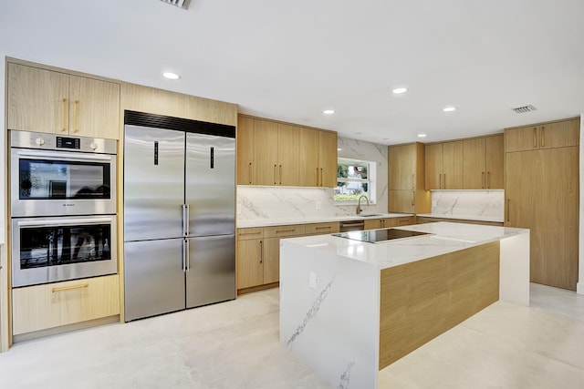 kitchen with a center island, light stone counters, backsplash, light brown cabinetry, and appliances with stainless steel finishes