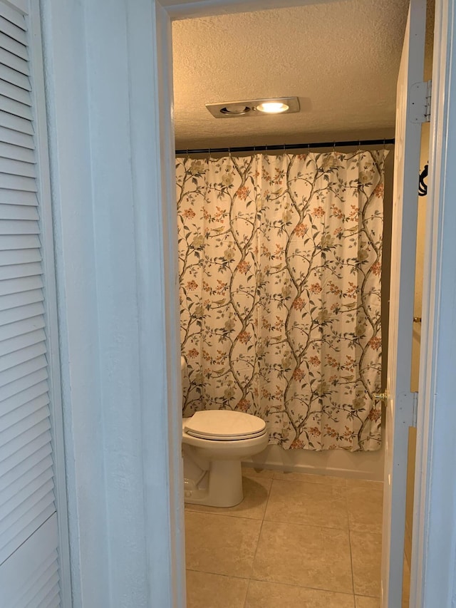 bathroom with tile patterned floors, toilet, shower / bath combo with shower curtain, and a textured ceiling