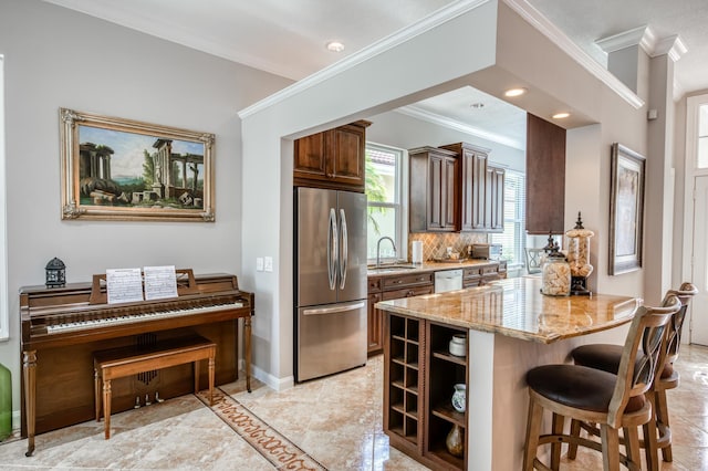 kitchen with kitchen peninsula, appliances with stainless steel finishes, light stone counters, a breakfast bar, and sink