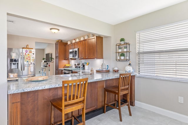 kitchen with light stone countertops, a kitchen bar, stainless steel appliances, and kitchen peninsula