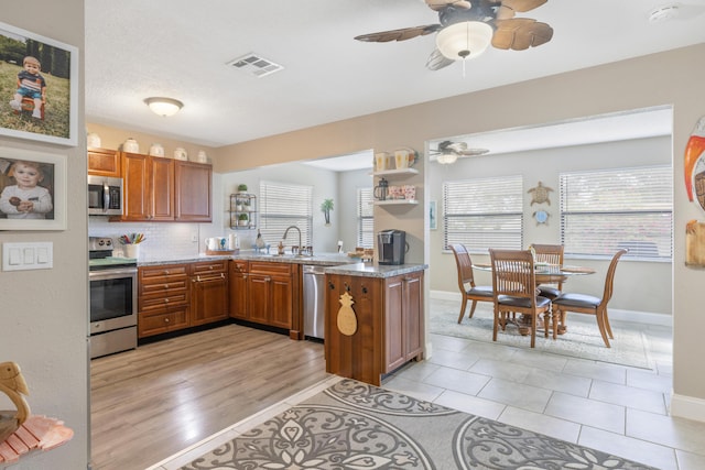 kitchen featuring sink, kitchen peninsula, decorative backsplash, light tile patterned floors, and appliances with stainless steel finishes