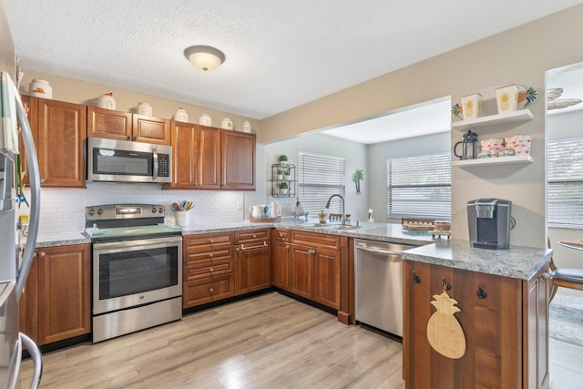 kitchen featuring light stone countertops, sink, light hardwood / wood-style flooring, kitchen peninsula, and appliances with stainless steel finishes