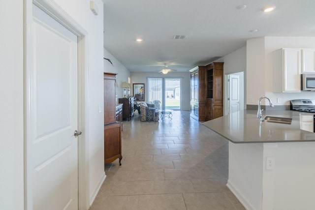 kitchen with kitchen peninsula, stainless steel appliances, ceiling fan, sink, and white cabinets