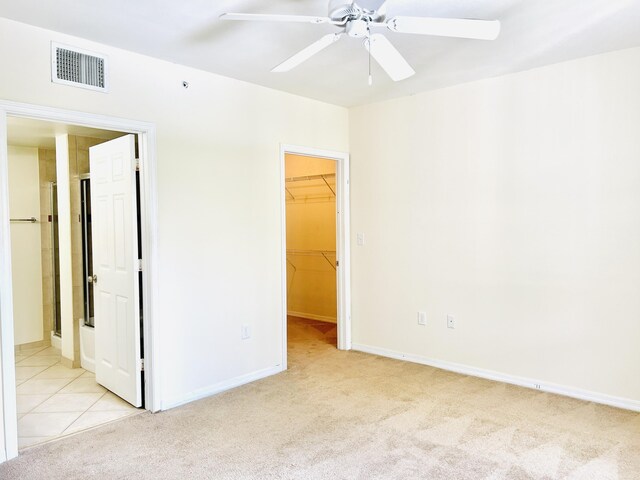 unfurnished bedroom featuring a spacious closet, a closet, ceiling fan, and light colored carpet