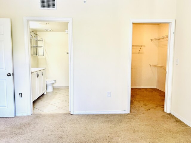 unfurnished bedroom with connected bathroom, light colored carpet, a spacious closet, and a closet