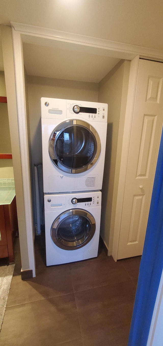 laundry area featuring stacked washer / dryer and dark tile patterned floors