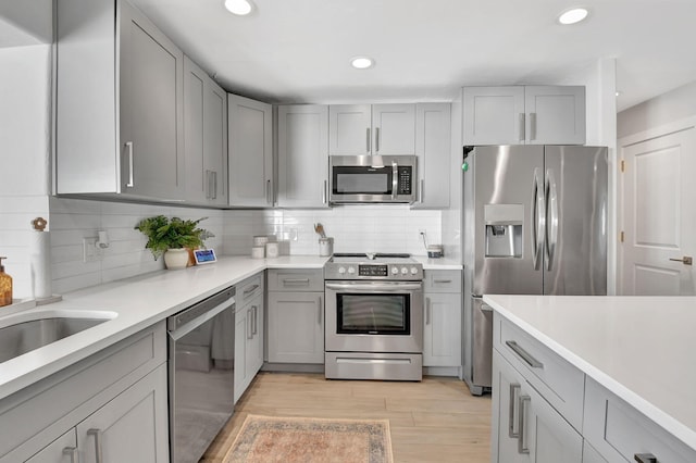 kitchen with backsplash, stainless steel appliances, light hardwood / wood-style flooring, and gray cabinetry