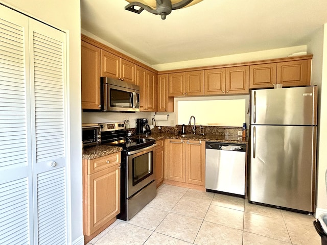 kitchen with dark stone countertops, sink, light tile patterned floors, and stainless steel appliances