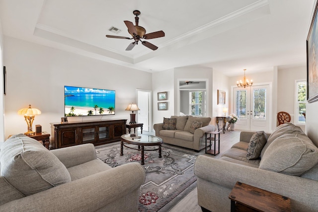 living room with a tray ceiling, crown molding, french doors, and ceiling fan with notable chandelier