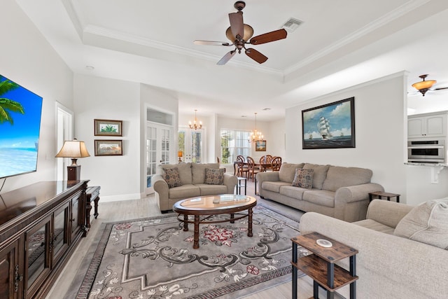 living room with hardwood / wood-style floors, ceiling fan with notable chandelier, a raised ceiling, and ornamental molding