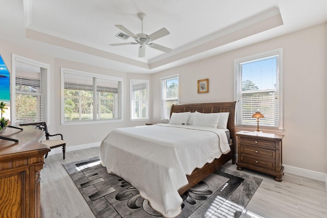 bedroom featuring ceiling fan, light wood-type flooring, ornamental molding, and a tray ceiling