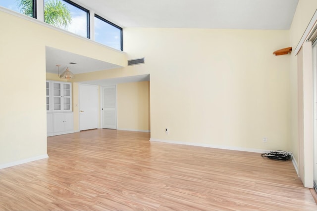 unfurnished room with high vaulted ceiling, light hardwood / wood-style flooring, and a notable chandelier