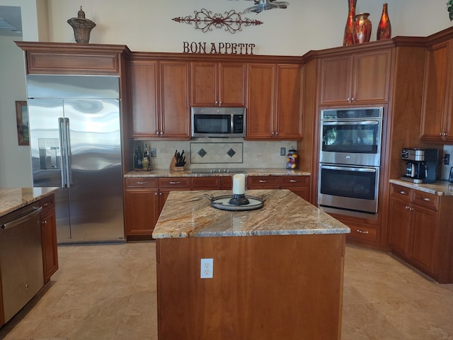 kitchen featuring tasteful backsplash, appliances with stainless steel finishes, brown cabinets, light stone counters, and a center island