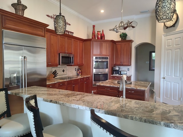 kitchen featuring arched walkways, a breakfast bar, stainless steel appliances, decorative backsplash, and ornamental molding