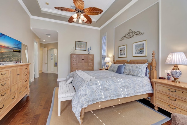 bedroom featuring baseboards, arched walkways, dark wood finished floors, a raised ceiling, and ornamental molding