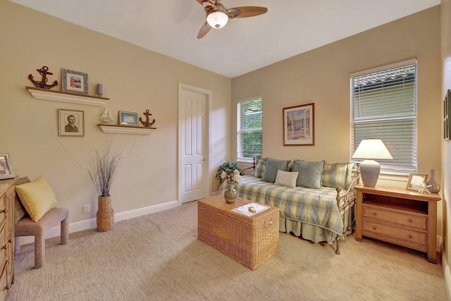 living area with a ceiling fan, light carpet, and baseboards