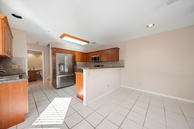 kitchen featuring sink, kitchen peninsula, decorative backsplash, light tile patterned flooring, and appliances with stainless steel finishes