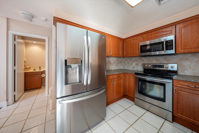 kitchen with dark stone counters, light tile patterned floors, appliances with stainless steel finishes, and tasteful backsplash