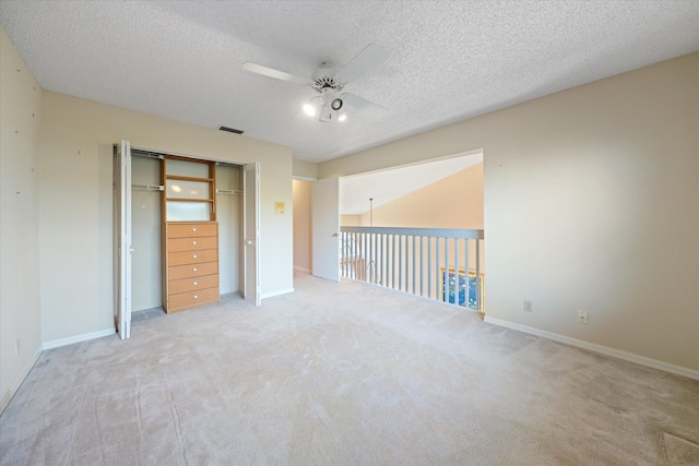 unfurnished bedroom featuring ceiling fan, light colored carpet, a textured ceiling, and a closet