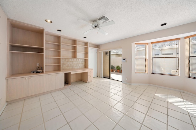 unfurnished living room with light tile patterned floors, built in desk, a textured ceiling, and ceiling fan