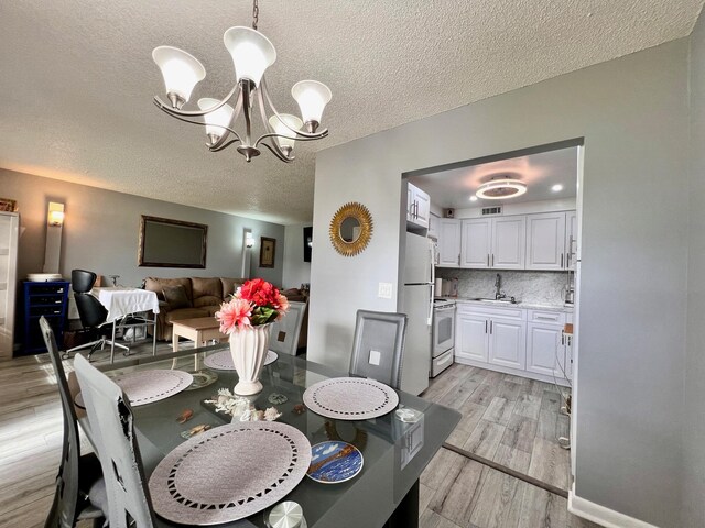 dining space with sink, an inviting chandelier, a textured ceiling, and light wood-type flooring