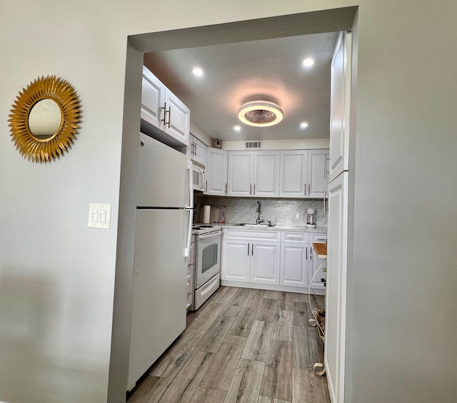 kitchen featuring white appliances, backsplash, sink, light hardwood / wood-style flooring, and white cabinetry