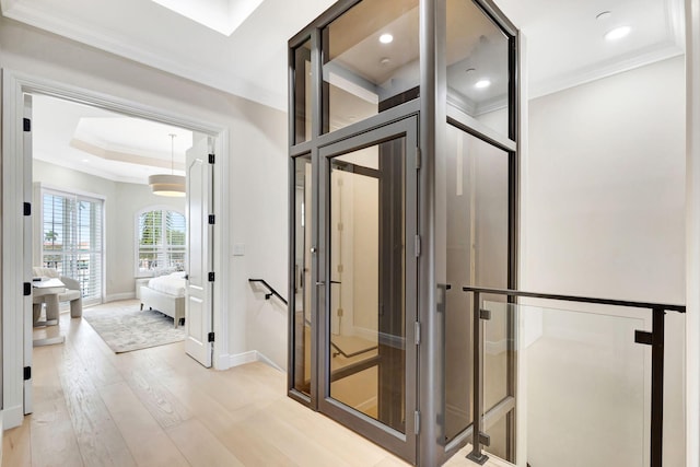 interior space featuring light wood-type flooring, a raised ceiling, and crown molding