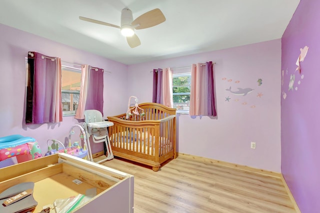 bedroom featuring ceiling fan, light hardwood / wood-style flooring, and a nursery area