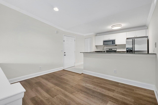 kitchen with kitchen peninsula, ornamental molding, stainless steel appliances, white cabinets, and hardwood / wood-style floors