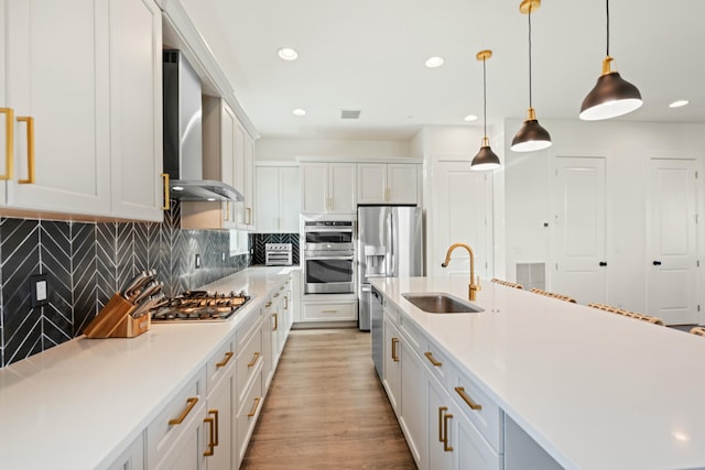 kitchen featuring appliances with stainless steel finishes, pendant lighting, sink, white cabinets, and wall chimney range hood