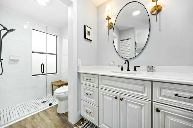 bathroom with hardwood / wood-style floors, vanity, toilet, and a shower with shower door