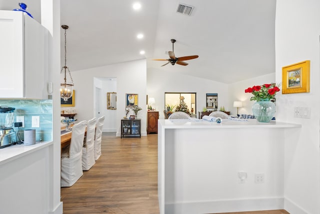 kitchen with lofted ceiling, kitchen peninsula, dark hardwood / wood-style floors, decorative light fixtures, and white cabinetry