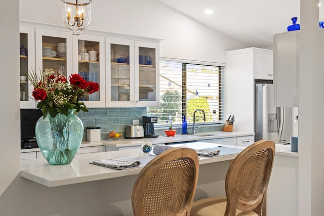 kitchen with kitchen peninsula, pendant lighting, vaulted ceiling, and white cabinetry