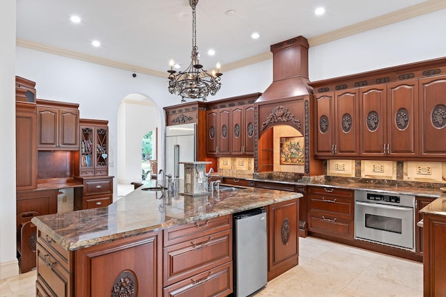 kitchen with dark stone counters, stainless steel appliances, sink, decorative light fixtures, and a center island with sink